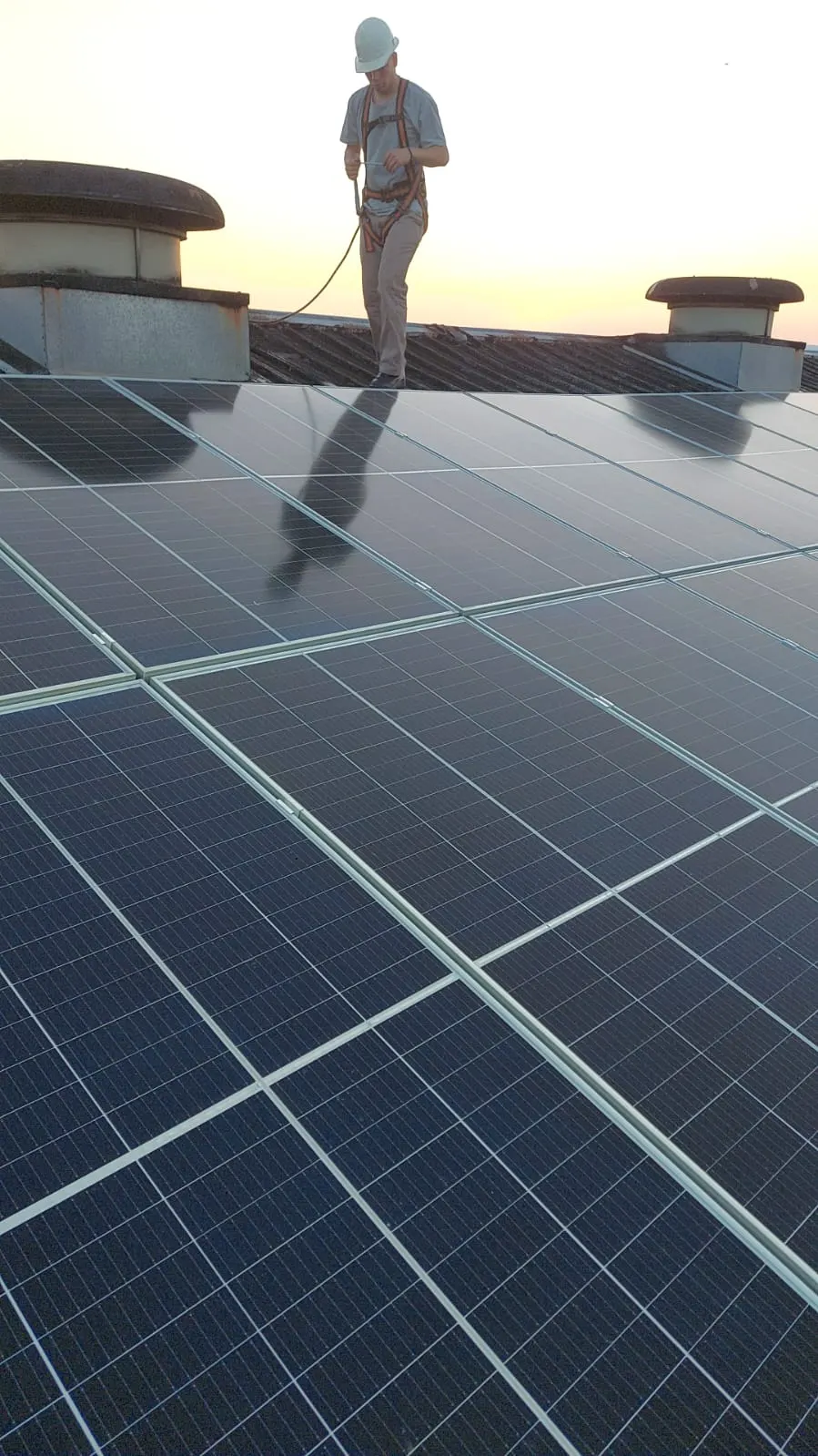 Instalador con arnés de seguridad trabajando sobre el techo al atardecer